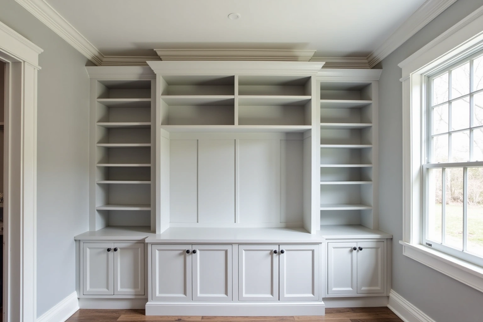 Pale grey painted built-in wall with open shelves each side, a central counter nook and lower cabinets with black knobs.
