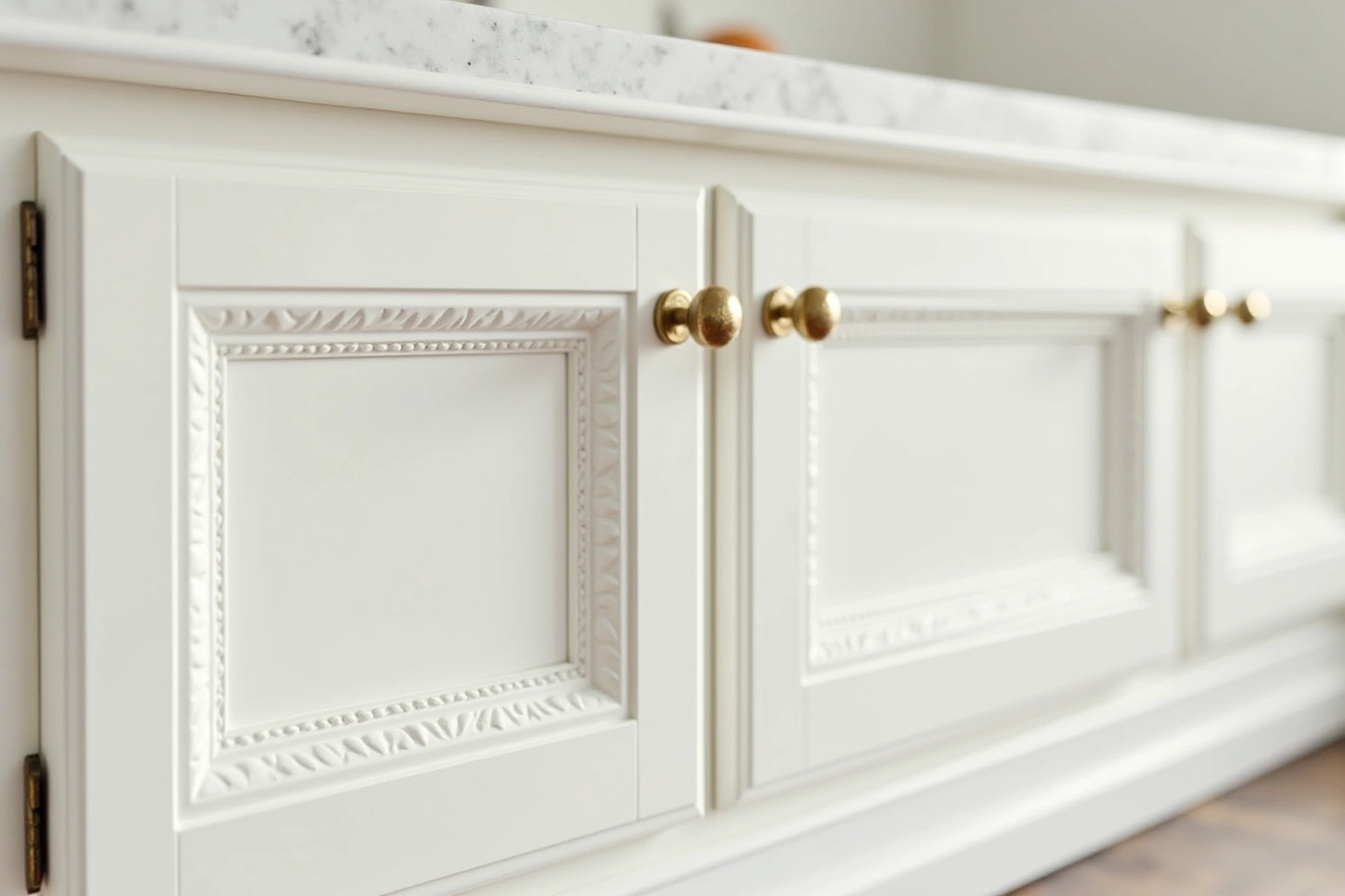 White inset cabinet doors with carved panel moulding, small brass knobs and exposed hinges below a marble counter.