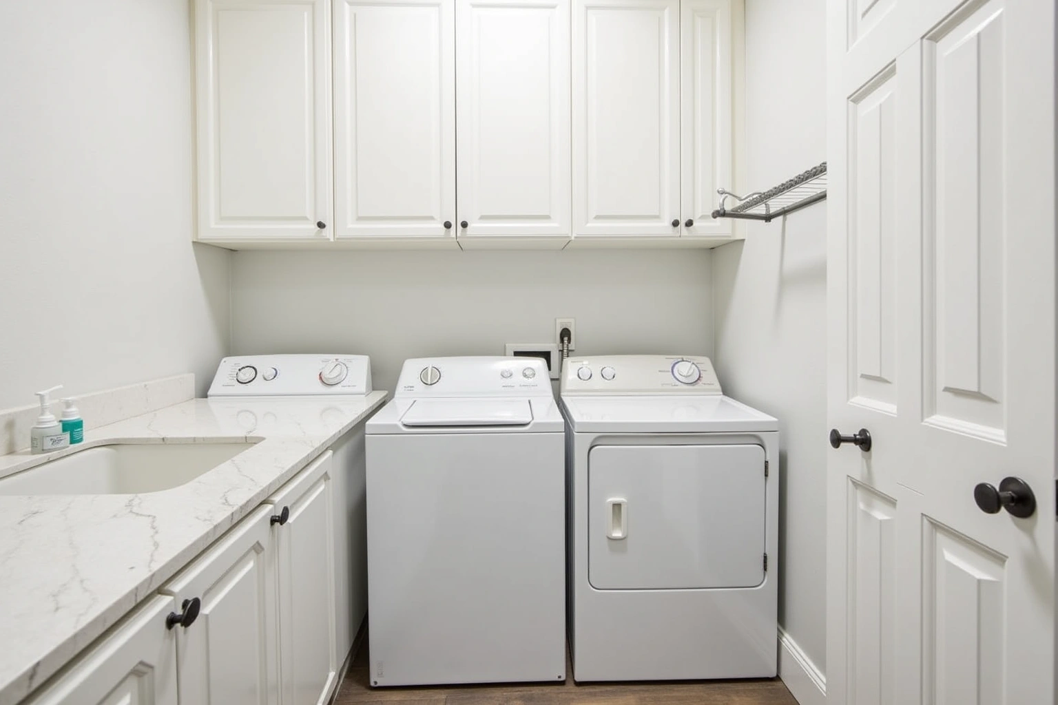 White raised-panel upper cabinets over a top-load washer and front-load dryer, with a marble folding counter and utility sink.