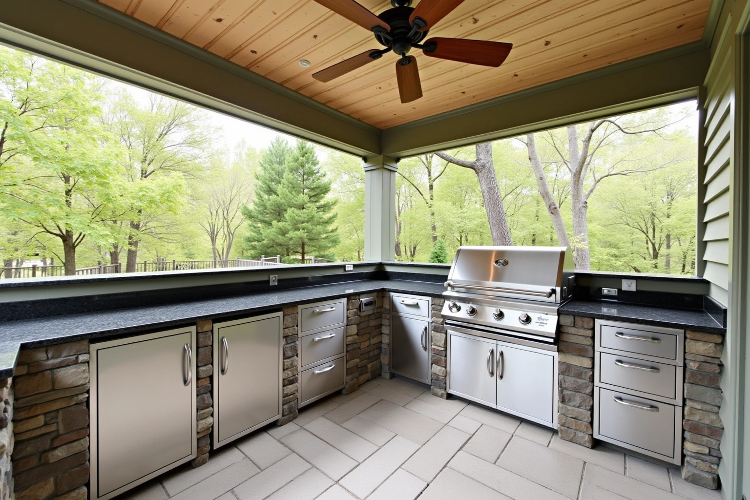 Stainless doors and drawers in a stone base under dark granite on a covered patio, with a built-in grill.